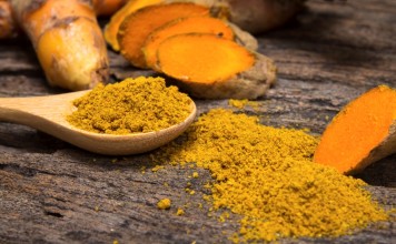 the turmeric powder in spoon and roots on wooden plate