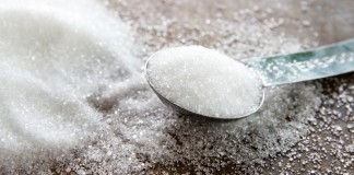 Close up of a pile of granulated sugar and a heaping teaspoon of sugar on a wood surface