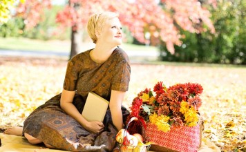 Happy woman sitting on a blanket in the park with baskets of apples and fall flowers