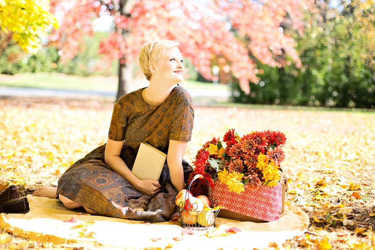 Happy woman sitting on a blanket in the park with baskets of apples and fall flowers