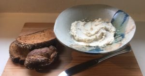 wooden cutting board topped with toast and a bowl of vegan cashew cream cheese substitute