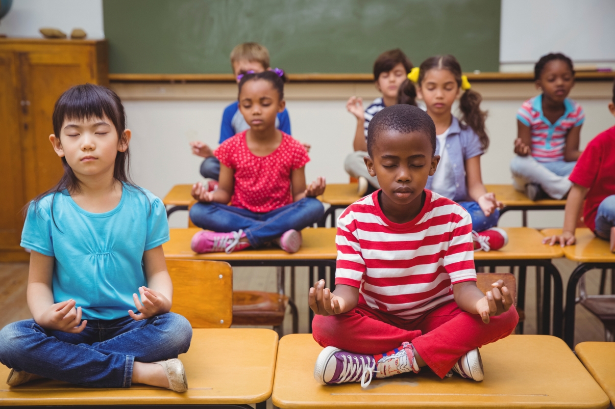 children sitting on top of their desks meditating