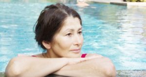 Woman in pool with folded arms resting on edge of pool