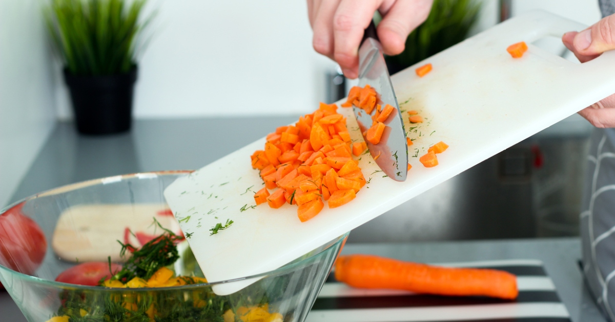 carrots being swept off a cutting board into a bowel of vegetables