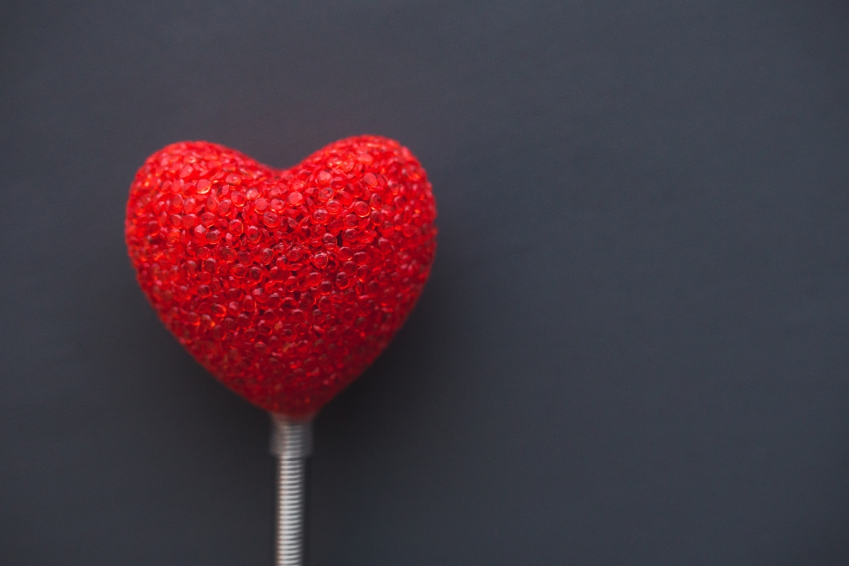 red plastic heart on a white stick with a gray background
