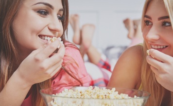 two friends, talking, smiling, and eating popcorn