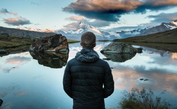 Man standing in a beautiful nature scene with the sky, rock formations, and a lake