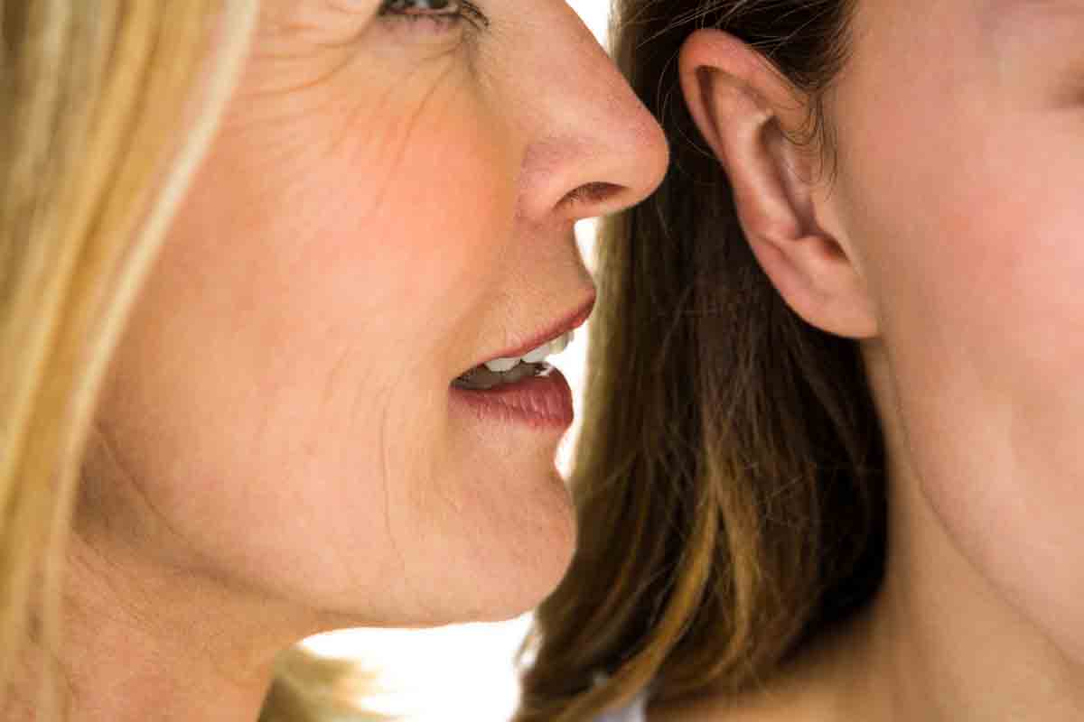 woman whispering into another woman's ear