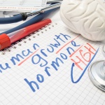 Note inscribed with Human Growth Hormone (HGH) or Somatotropin is surrounded by laboratory test tube with blood, brain figure and stethoscope. Significance and effects of growth hormone on human body