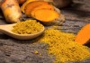the turmeric powder in spoon and roots on wooden plate