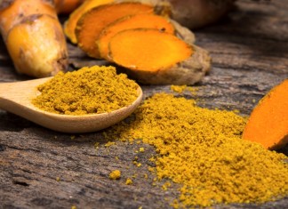 Turmeric Offers New Hope for Lupus Sufferers the turmeric powder in spoon and roots on wooden plate