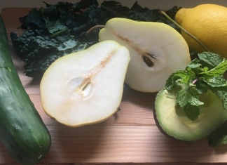 cutting board with cucumber, pear, avacado, lemon, and herbs