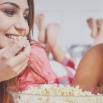 two friends, talking, smiling, and eating popcorn