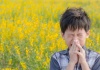 boy standing in a field of flowers sneazing
